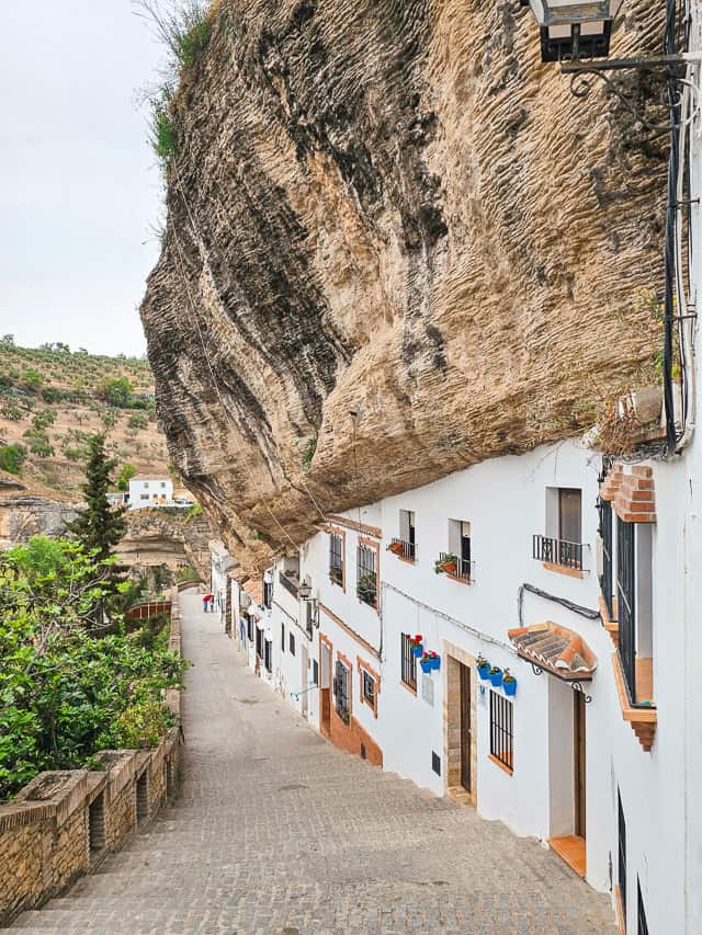 Buildings appear to support or grow into a slanting cliffside. Calle Calcetas
