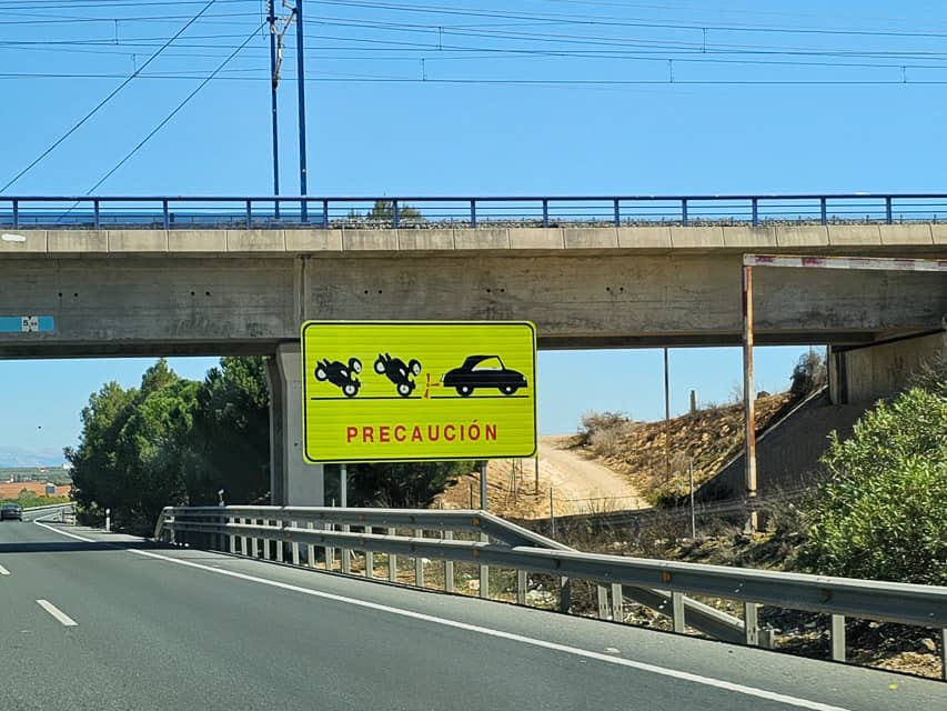 A yellow sign shows motorcycles tailgating a car, cautioning motorists to practice safe driving.