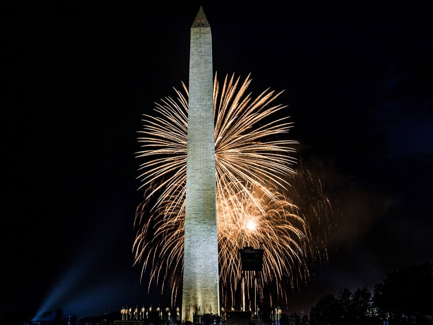 White fireworks explode over the Washington Monument.