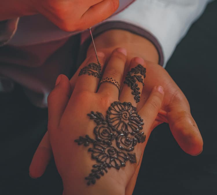 A woman is getting black henna designs applied to her hand.