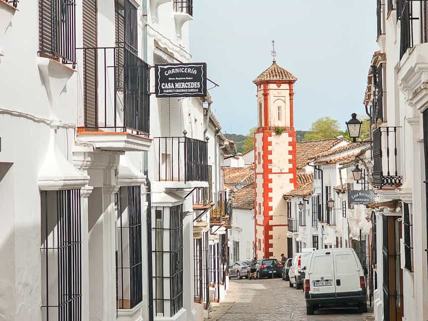 A view down a little street in Grazalema - white buildings with wrought iron black windows, and the red and white tower of a church is framed perfectly between the streets.