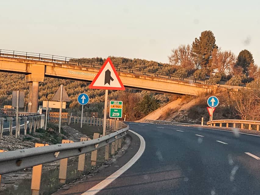 A Spanish merge sign. A white triangle with red border. A black line intersects a larger black arrow at an angle.