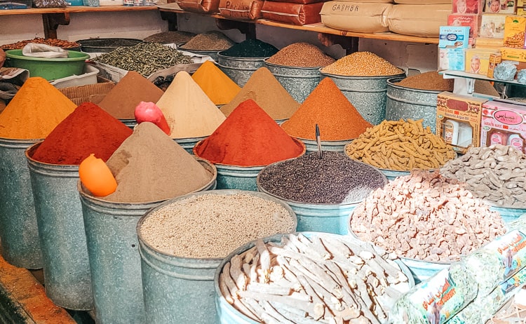 Bins piled high with colorful spices are displayed in a spice shop - the spices making a conical shape at the top of each bin.