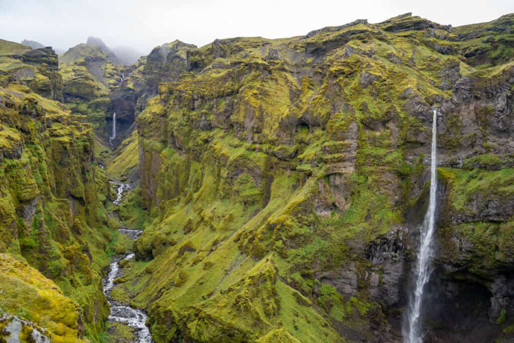 A very tall mountain wall with with 2 waterfalls with the water cascading now the cliff.