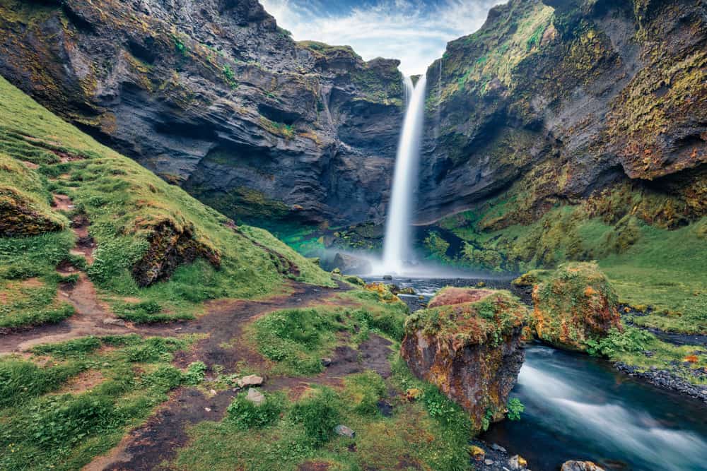 A waterfall crashes down into a turquoise pool that goes into a river.