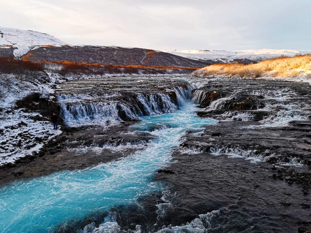 Multiple little waterfalls go down into a beautiful blue stream.