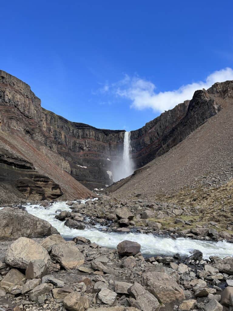 A tall waterfall crashes down and goes down into the rivers with rocks on both sides.