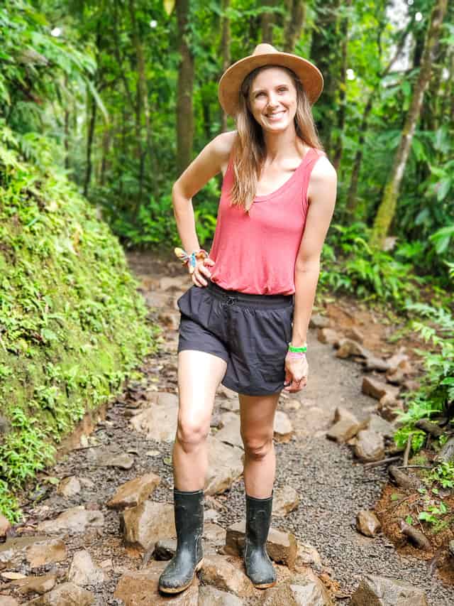 Woman stands on trail, with trees behind her.