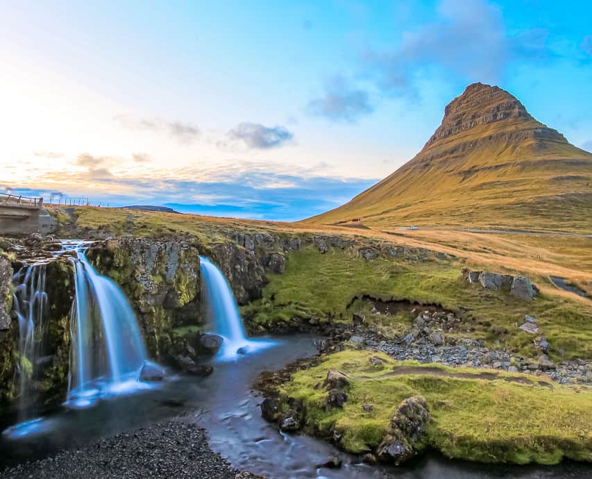 A few very blue waterfalls with a beautiful multicolored sky with a very tall stone tower.