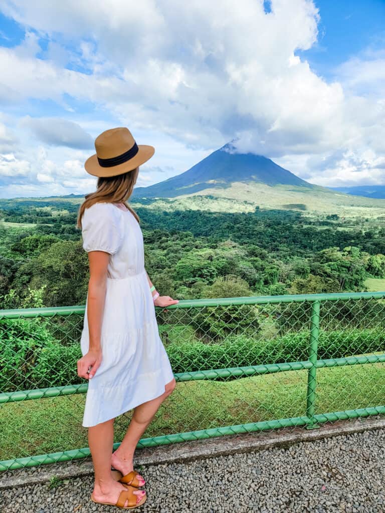 A woman in a white dress looks off at Arenal Volcano which is one of the gems of the area
