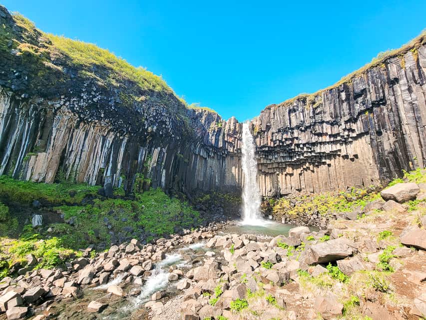 A waterfall goes down into a greenish pool.
