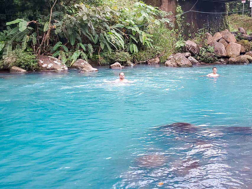 2 guys are swimming in a milky blue river.