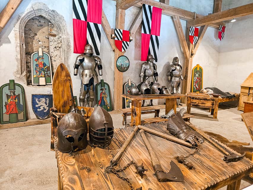 A room inside the castle that has lots of medieval paintings and armor such as helmets and axes.