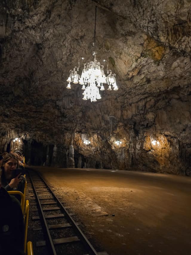 A yellow cart goes on tracks through a rock cavern with a extravagant glass chandelier