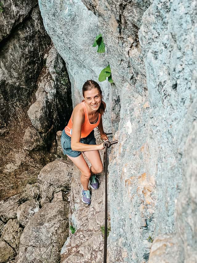 Woman climbs up narrow ledge holding on to a chain attached to the wall.