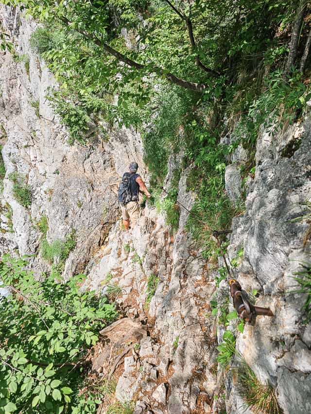 Man walks along a narrow ledge, holding on to a chain to get to the source of the Soca.