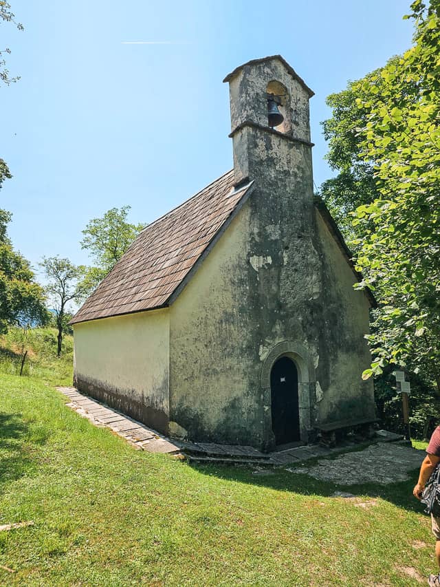 A stone and wood church in a grassy field and trees.