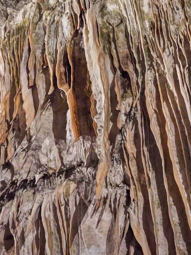 There are lots of sheets of stalactites on a cave rock walls.