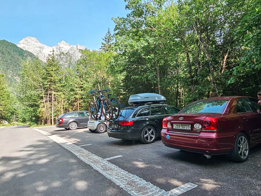 Multiple cars park by trees with mountains in the distance.