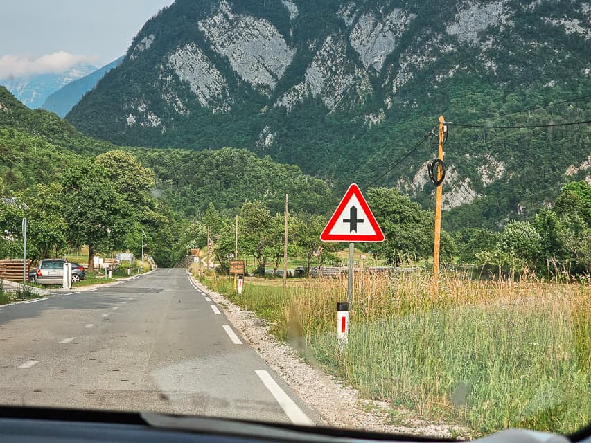 A street view out of a car window, with a triangle sign lined in red, with a t-like symbol in the middle of it.