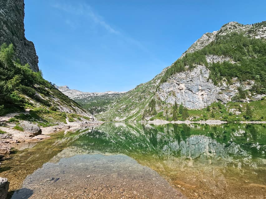 The view at the edge of the water of a reflective lake with mountains circling the lake.