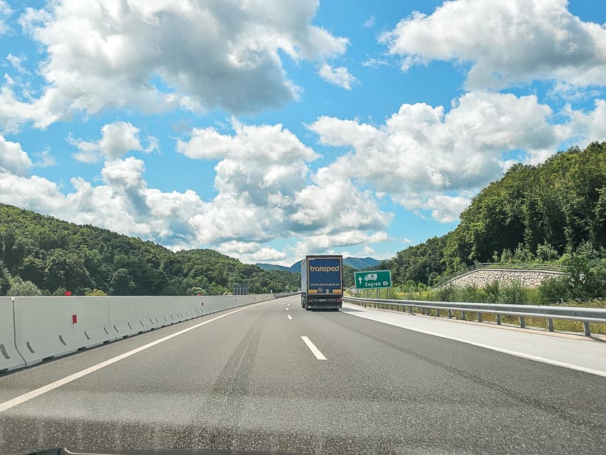 A highway in Slovenia, that goes around the corner with trees on either side.