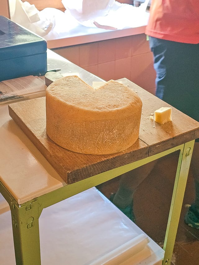 A large dark orange wheel of cheese with a triangle missing on a wood plaque.