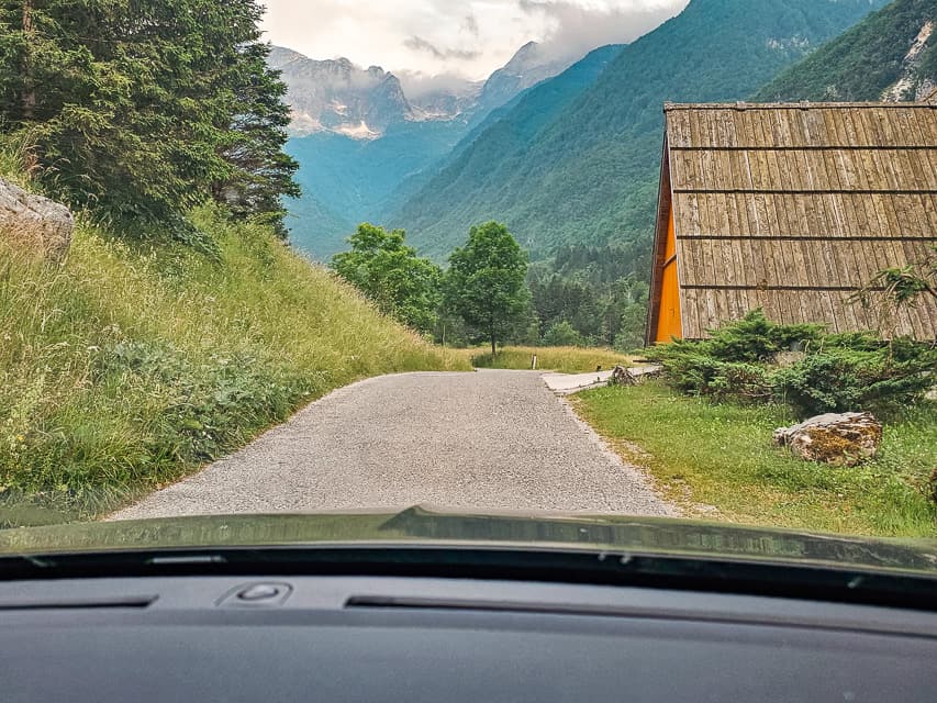 Small country road with a building wiht a tall sloped roof along it and mountains in the distance.