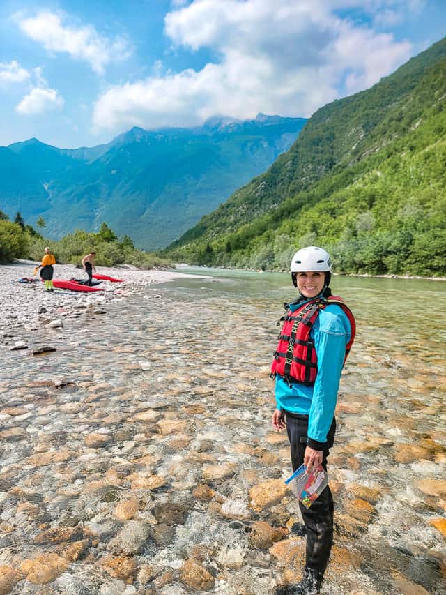 A woman stands in ankle deep clear water on the Soča River.
