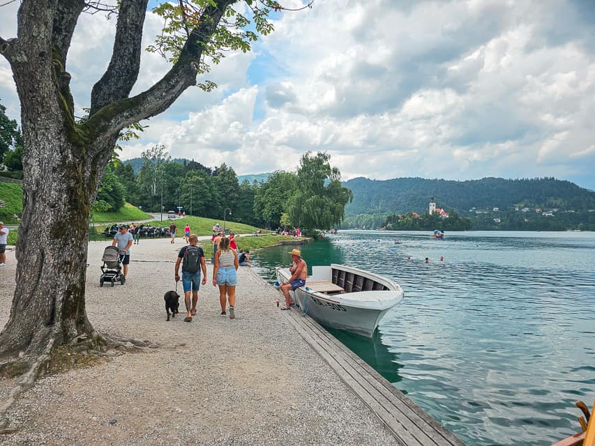 People walk along a gravel sidewalk along the lakeside.