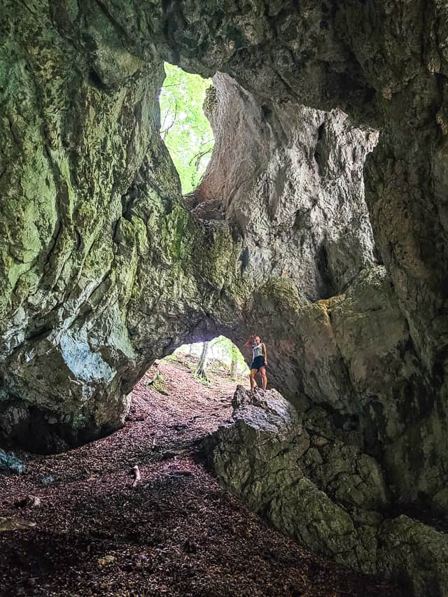 A woman stands on a tall rock in a cave looking at the shear walls with holes in the middle.