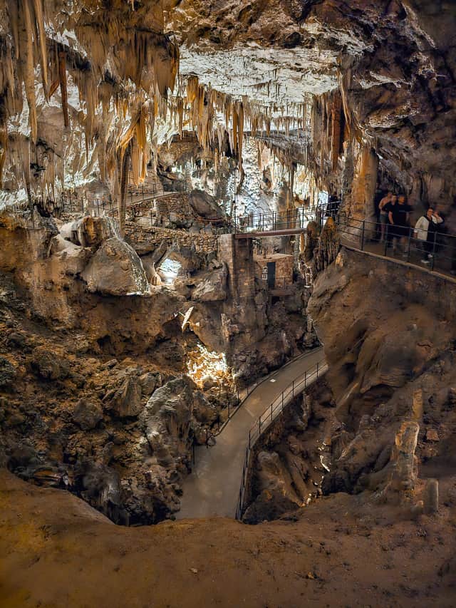 A cement path wind through the cavern of Postojna Cave with stalactites coming out of the ceiling