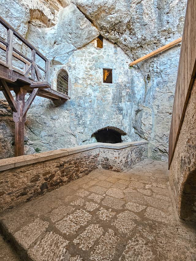 The back of the castle that backs up to the side of the cliff, with a bridgethat enters the cave behind.