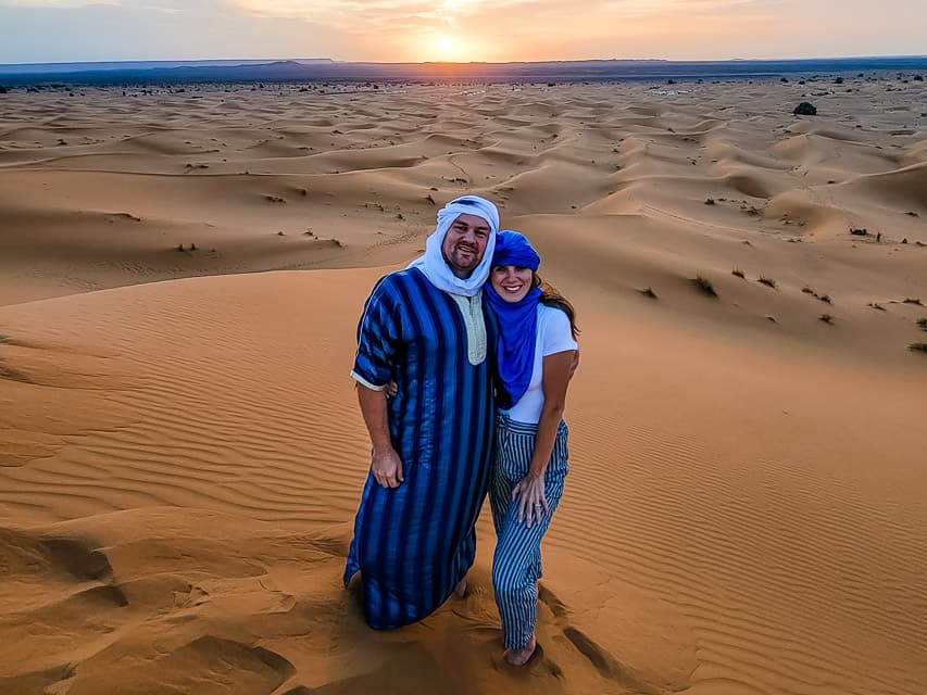 A man and woman stand together romantically in a sunset on a Sahara desert