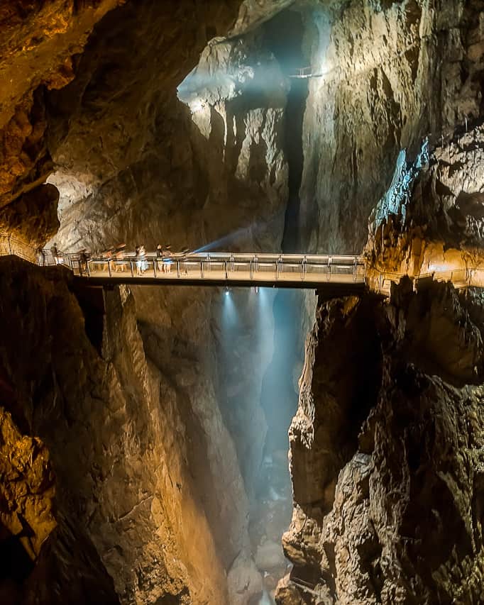A long bridge goes from two sides of the sheer rock cliffs. There are people on the bridge looking at the large drop .