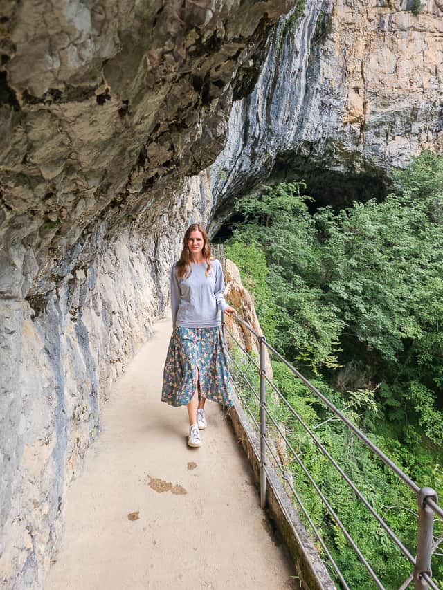 A woman stand on a pathway looking over a rock overhang and rock ceiling.