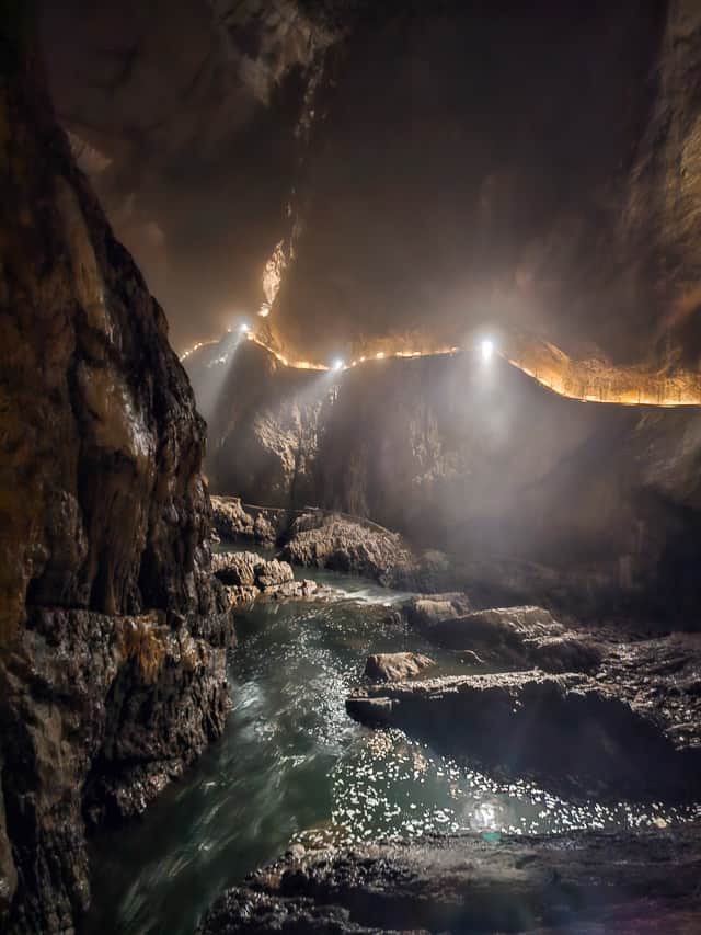 In a cave a waterfall goes down over a drop and out of sight. This is a super cool cave in slovenia