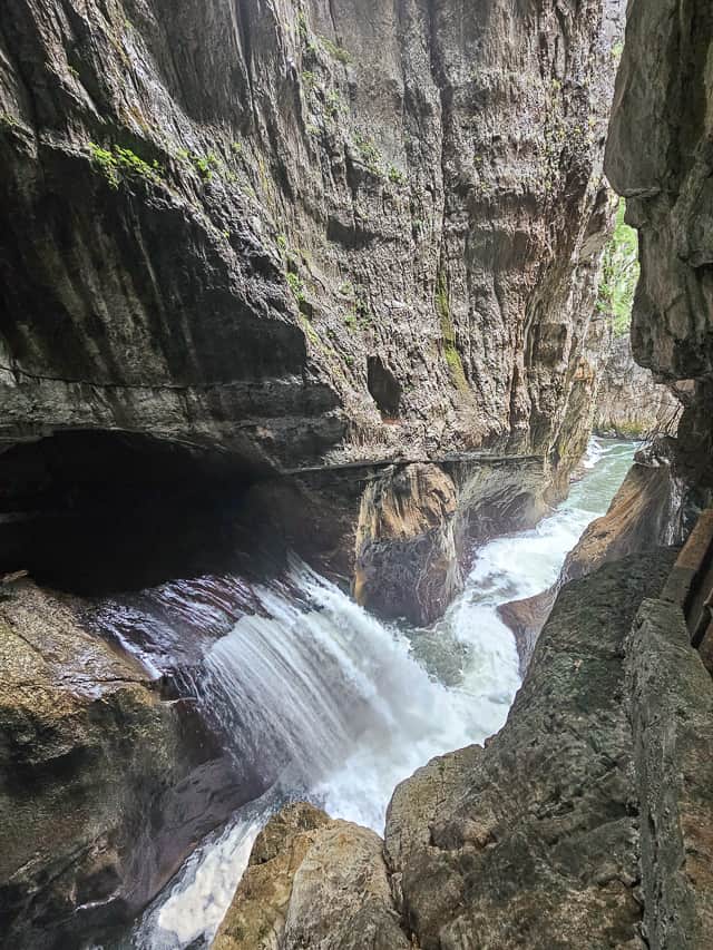 Water crashes out of the ricks into a rushing white water river with a small rock canyon.