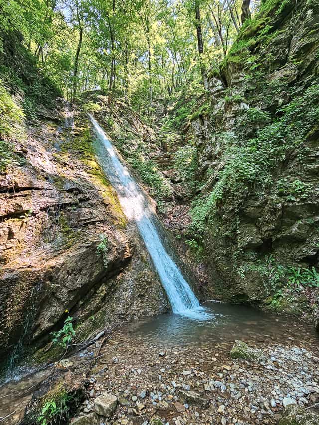 A small waterfall with blue water into a large pool of water with small rocks.