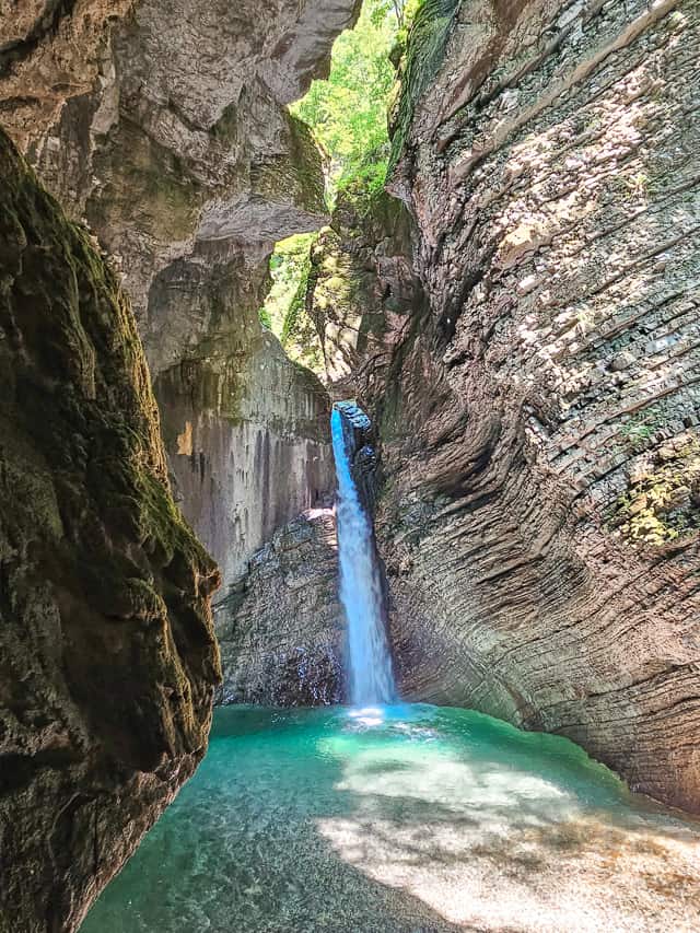 A waterfall drops through a canyon with tall curving walls into a pool of turquoise water.