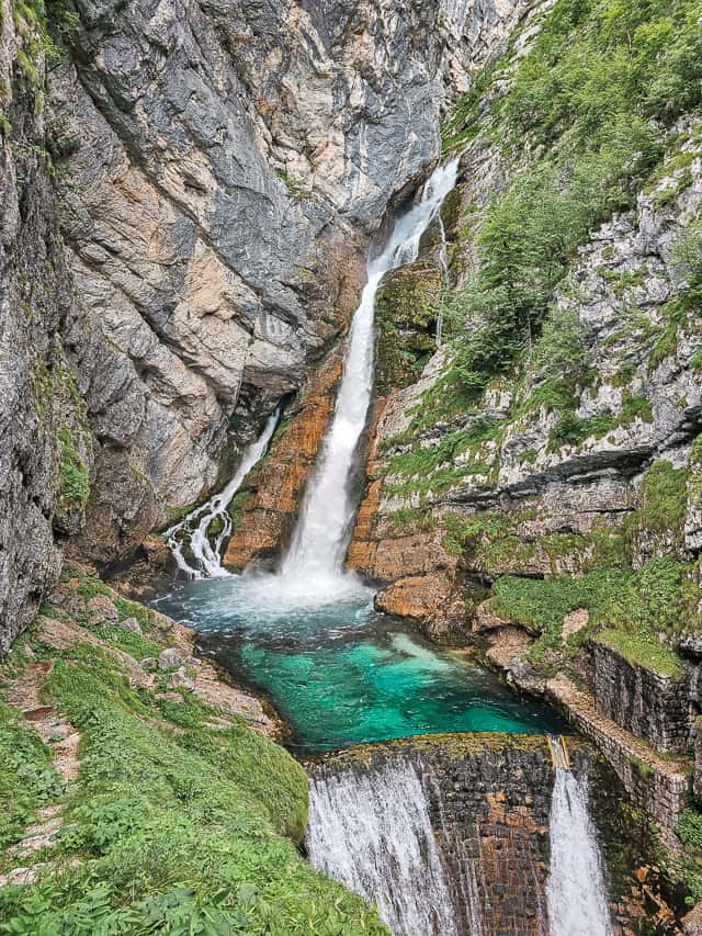 Multiple streams of the Savica waterfall go down into a deep turquoise pool and is allowed out by a dam.
