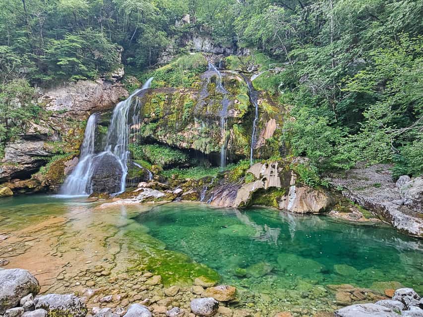 Multiple streams cascade down a rocky cliff, ending in a gorgeous deep turquoise pool - slap virje is one of the most beautiful waterfalls in slovenia.