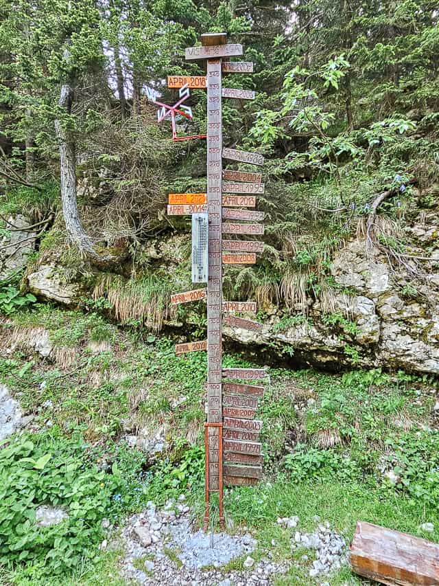 A pole on the path with wood markers attached to the side showing the snowfalls on the trail.