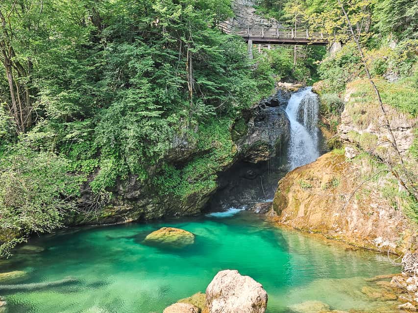 A waterfall goes down into a turquoise pool with a bridge above it.