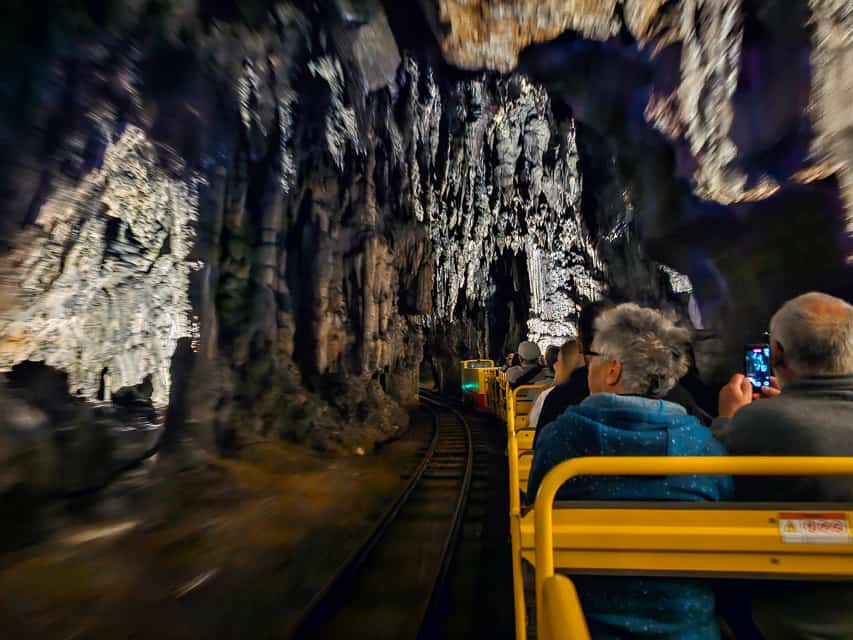 A yellow cart on metal tracks with takes people through the cavern filled stalagmites and stalactites.