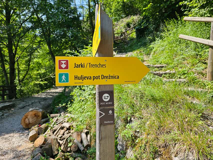 A yellow wood sign leads to where there are WW1 trenches. with the tail continuing to the left of the sign.