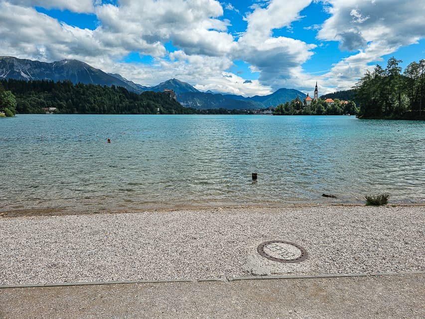 A stone beach opens up to the water in Lake Bled with an island in the distance.
