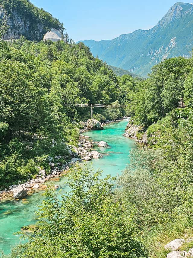 The views from the trail of the turquoise Soca river with ferns and trees all around it.