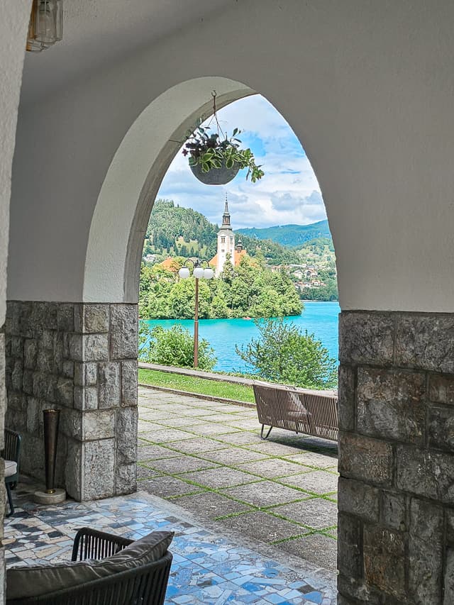 A stone archway lets you see a beautiful view of an island in the middle of a blue lake.