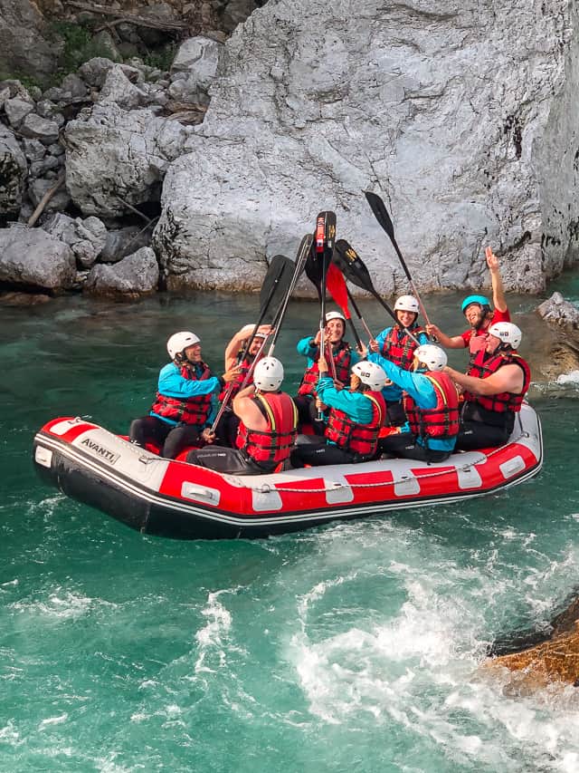 A group of 9 people put their paddles together in the middle of the Soča River.